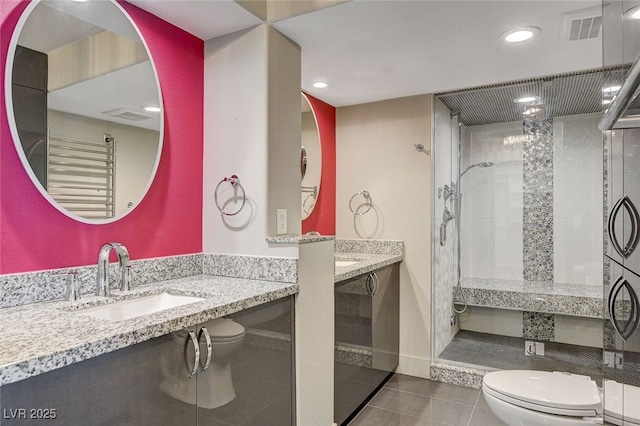 bathroom with toilet, vanity, tile patterned flooring, and tiled shower