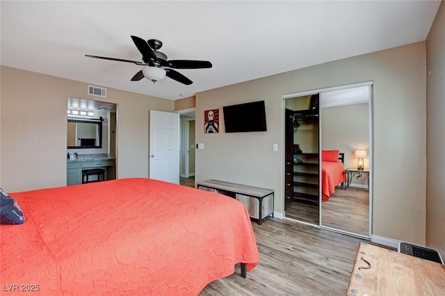 bedroom featuring light wood-type flooring, a closet, ensuite bathroom, and ceiling fan