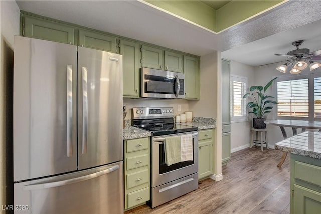 kitchen featuring appliances with stainless steel finishes, green cabinets, light stone counters, and light hardwood / wood-style floors