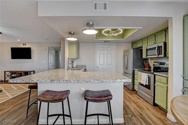 kitchen with appliances with stainless steel finishes, hardwood / wood-style flooring, green cabinets, a breakfast bar, and kitchen peninsula