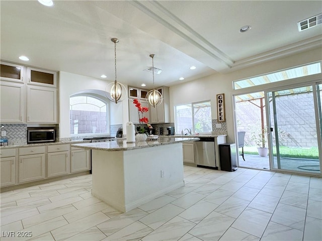 kitchen with hanging light fixtures, stainless steel appliances, light stone countertops, decorative backsplash, and a center island