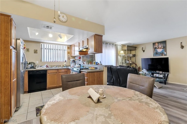 kitchen featuring stainless steel refrigerator, a tray ceiling, light tile patterned floors, sink, and black dishwasher