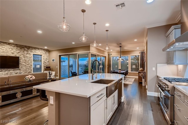 kitchen featuring a center island with sink, wall chimney exhaust hood, range with two ovens, and pendant lighting