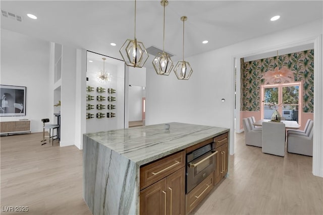 kitchen featuring light stone counters, light wood-type flooring, a center island, wall oven, and hanging light fixtures