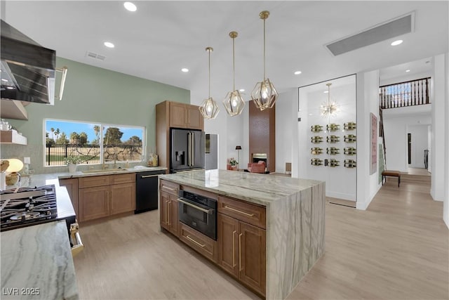 kitchen with light stone countertops, extractor fan, black appliances, pendant lighting, and a kitchen island