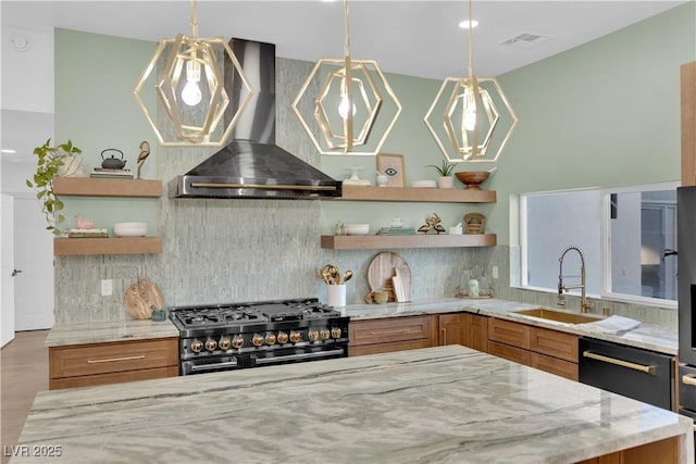 kitchen featuring hanging light fixtures, range with two ovens, light stone counters, wall chimney range hood, and sink