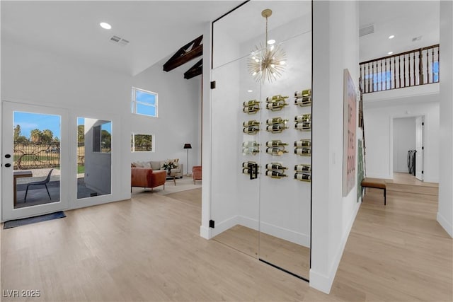 interior space featuring light wood-type flooring, beam ceiling, a notable chandelier, and a towering ceiling