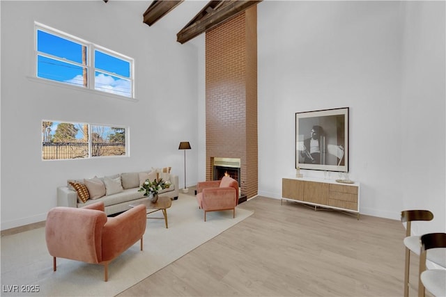 living area with beam ceiling, light hardwood / wood-style floors, a brick fireplace, and a towering ceiling