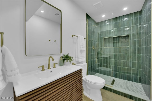 bathroom featuring vanity, a tile shower, and toilet