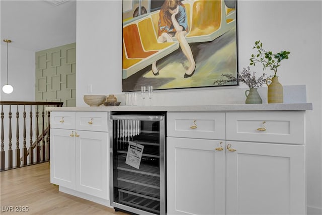 bar with light wood-type flooring, white cabinets, wine cooler, and decorative light fixtures