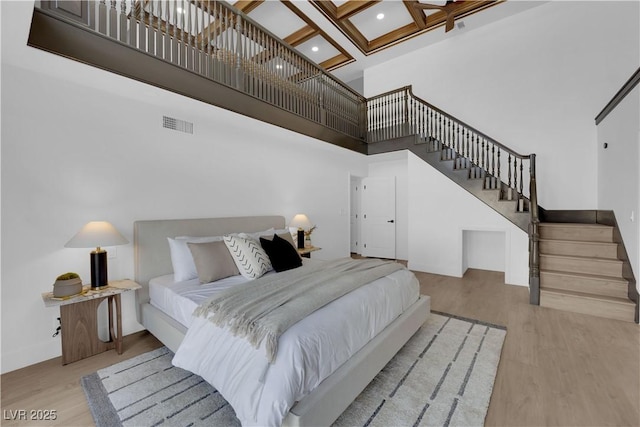 bedroom featuring beam ceiling, light hardwood / wood-style floors, a high ceiling, and coffered ceiling