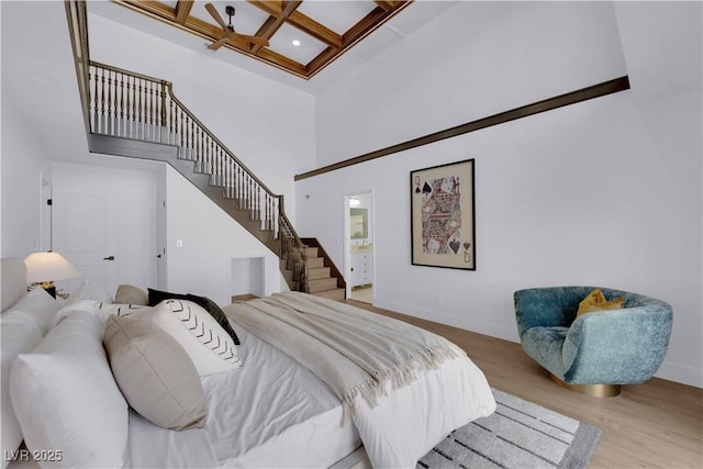 bedroom with coffered ceiling, light wood-type flooring, ensuite bathroom, a high ceiling, and beam ceiling