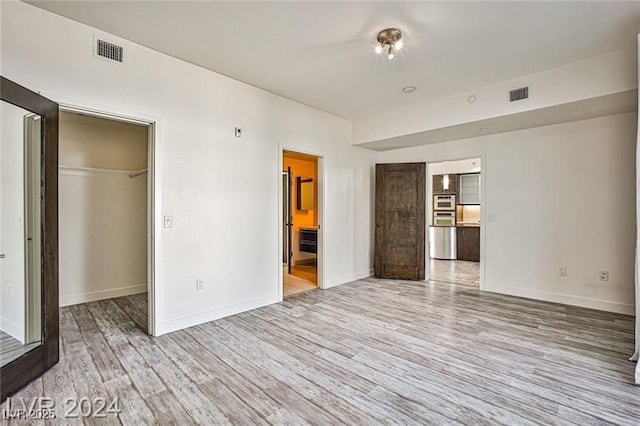 unfurnished bedroom featuring a closet, connected bathroom, a walk in closet, and light hardwood / wood-style flooring