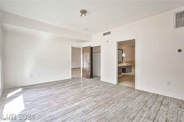 unfurnished bedroom featuring a closet, connected bathroom, and light hardwood / wood-style floors