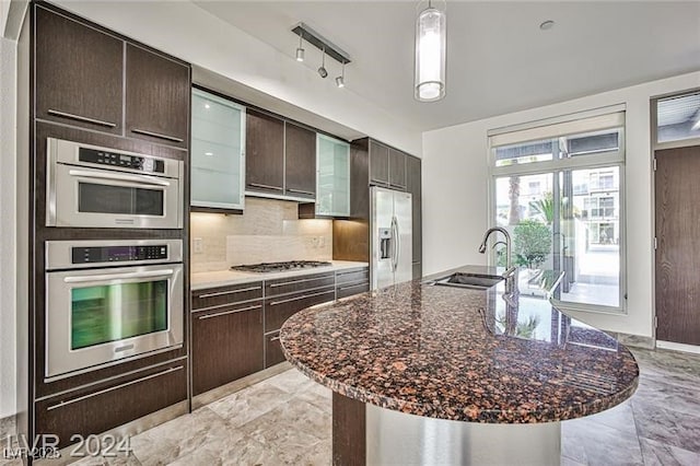 kitchen with an island with sink, stainless steel appliances, dark brown cabinetry, sink, and backsplash