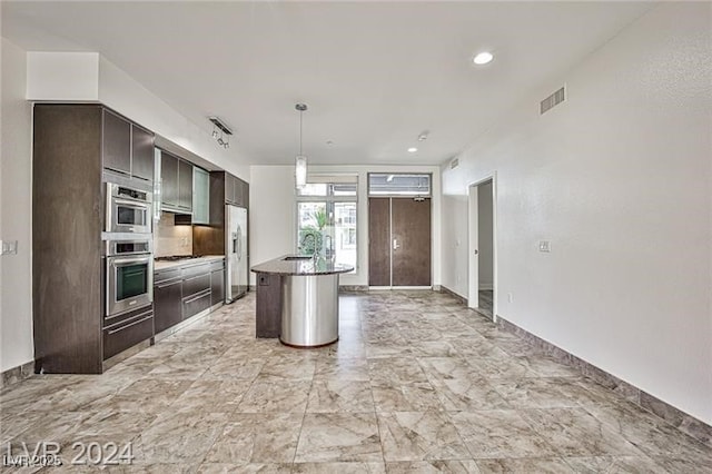 kitchen featuring a center island with sink, decorative light fixtures, dark brown cabinetry, and stainless steel fridge