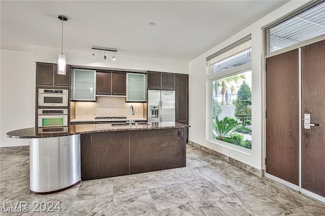 kitchen with dark brown cabinets, dark stone counters, stainless steel refrigerator with ice dispenser, pendant lighting, and sink