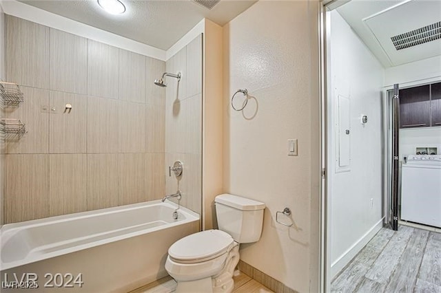 bathroom with washer / clothes dryer, hardwood / wood-style flooring, tiled shower / bath, and toilet