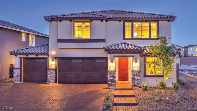 mediterranean / spanish-style house with decorative driveway, a tile roof, stucco siding, a garage, and stone siding