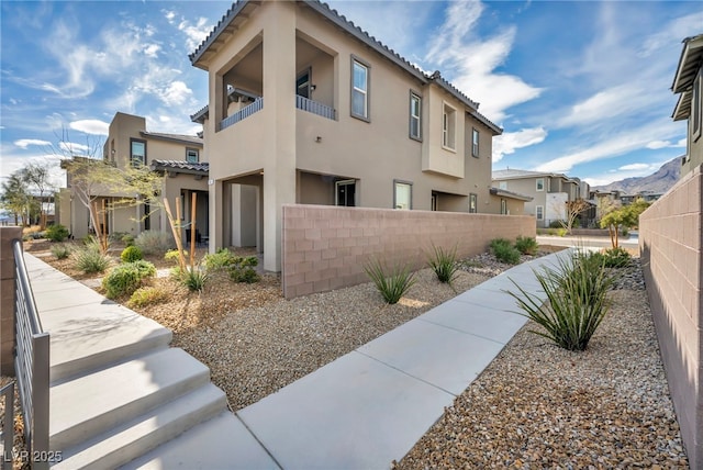 view of side of home featuring a residential view, stucco siding, a tile roof, and fence