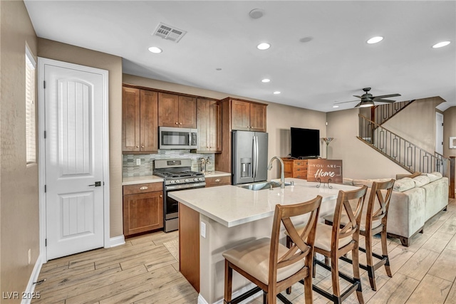 kitchen featuring visible vents, light wood-style flooring, decorative backsplash, appliances with stainless steel finishes, and a kitchen breakfast bar