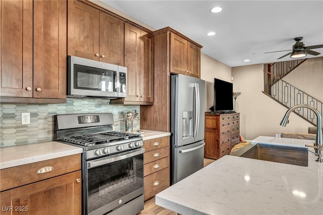 kitchen with brown cabinetry, decorative backsplash, appliances with stainless steel finishes, and a sink