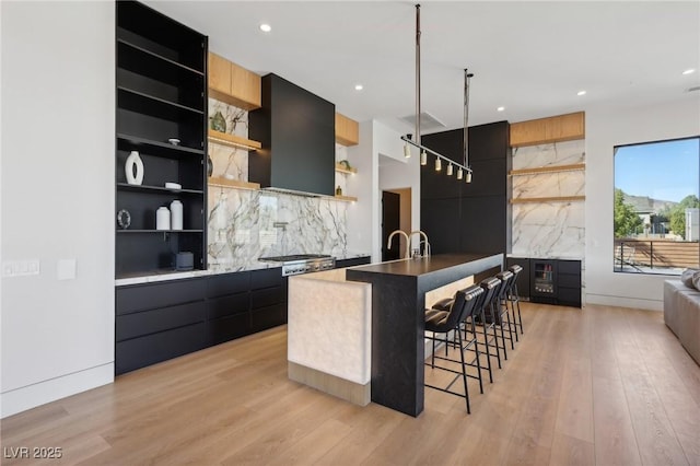 bar with exhaust hood, stainless steel gas stovetop, light wood-type flooring, and tasteful backsplash