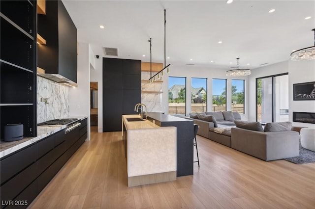 kitchen featuring a center island with sink, stainless steel gas stovetop, light hardwood / wood-style floors, pendant lighting, and sink