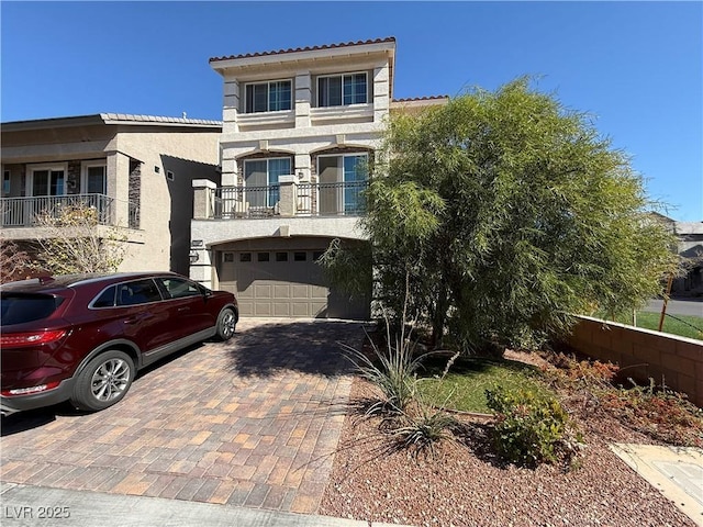 mediterranean / spanish house featuring decorative driveway, a tile roof, stucco siding, a balcony, and a garage