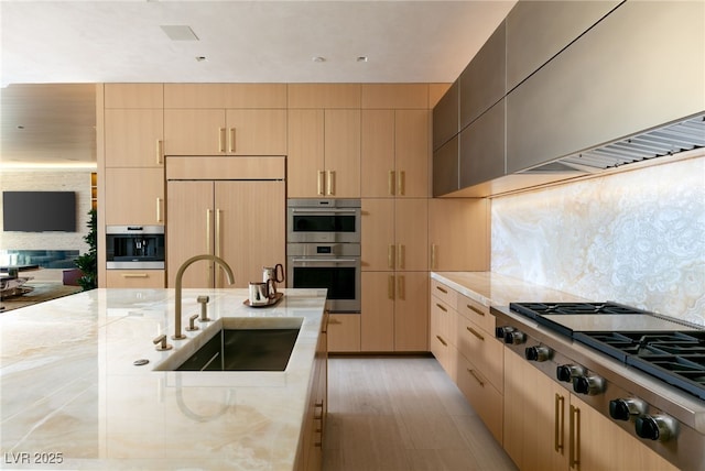 kitchen with appliances with stainless steel finishes, sink, light stone counters, light brown cabinetry, and decorative backsplash