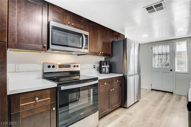 kitchen with appliances with stainless steel finishes, light hardwood / wood-style floors, and dark brown cabinetry