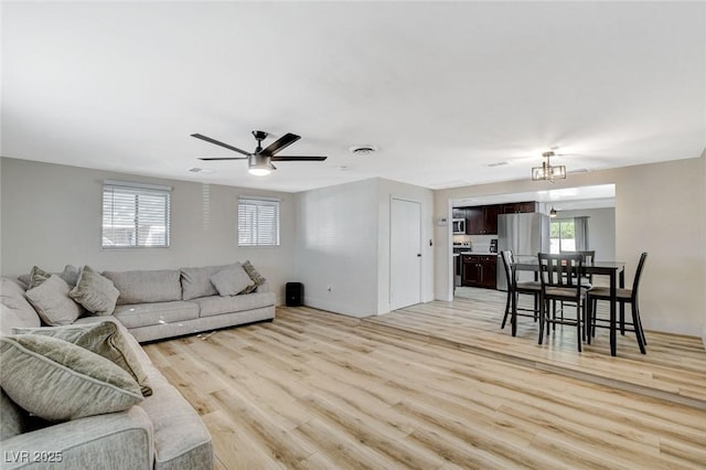 living room featuring ceiling fan with notable chandelier and light hardwood / wood-style flooring