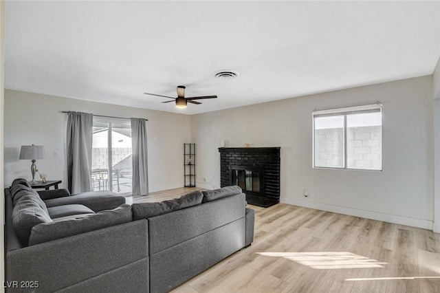 living room featuring ceiling fan, light hardwood / wood-style flooring, and a brick fireplace