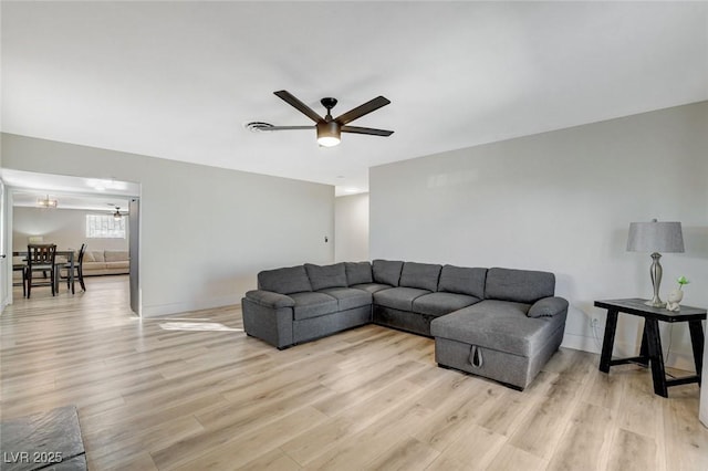 living room featuring ceiling fan with notable chandelier and light wood-type flooring