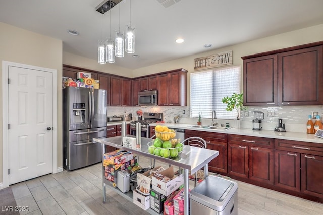 kitchen featuring appliances with stainless steel finishes, sink, hanging light fixtures, an island with sink, and tasteful backsplash