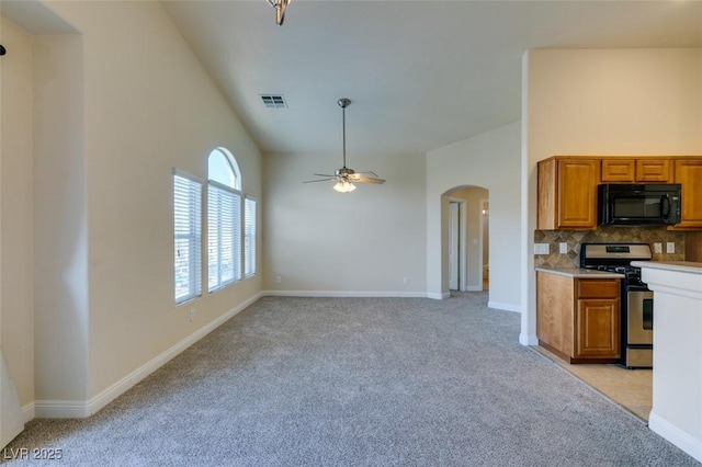 kitchen featuring a towering ceiling, ceiling fan, stainless steel gas range, light carpet, and decorative backsplash