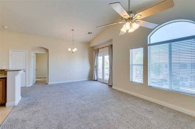 carpeted empty room featuring ceiling fan with notable chandelier and lofted ceiling