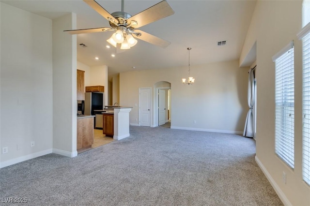 unfurnished living room featuring a high ceiling, light carpet, and ceiling fan with notable chandelier