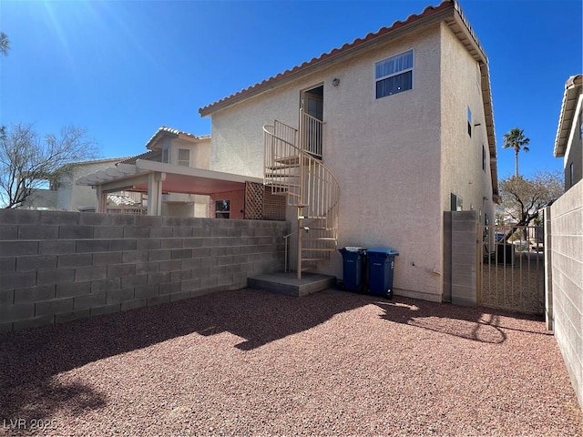 back of property featuring fence, a tiled roof, and stucco siding