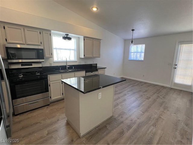 kitchen with dark countertops, appliances with stainless steel finishes, a center island, vaulted ceiling, and a sink