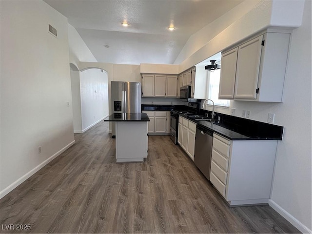 kitchen featuring a center island, lofted ceiling, dark countertops, appliances with stainless steel finishes, and a sink