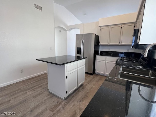 kitchen with stainless steel fridge, visible vents, white cabinets, lofted ceiling, and a kitchen island