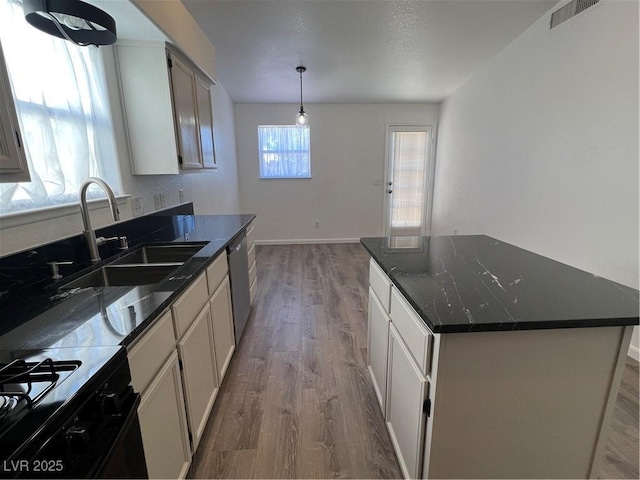 kitchen featuring visible vents, dishwasher, decorative light fixtures, a center island, and a sink
