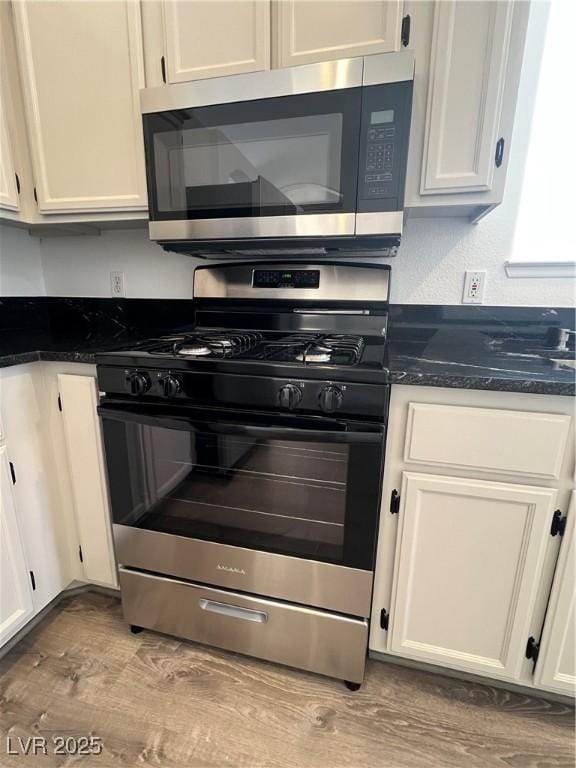 kitchen with white cabinets, light wood-type flooring, dark stone counters, and stainless steel appliances