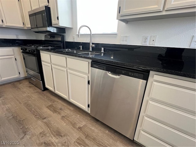 kitchen with dark stone counters, stainless steel appliances, a sink, and white cabinetry