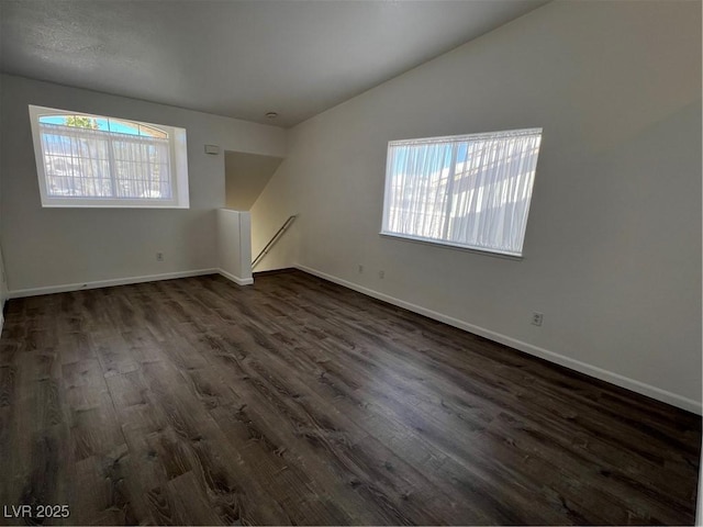 empty room featuring baseboards, vaulted ceiling, and dark wood-style flooring