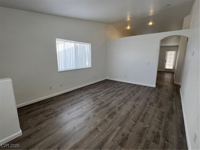 spare room featuring arched walkways, baseboards, lofted ceiling, and dark wood-style floors