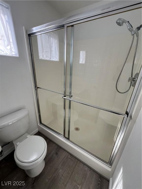 bathroom with a shower stall, toilet, and wood finished floors
