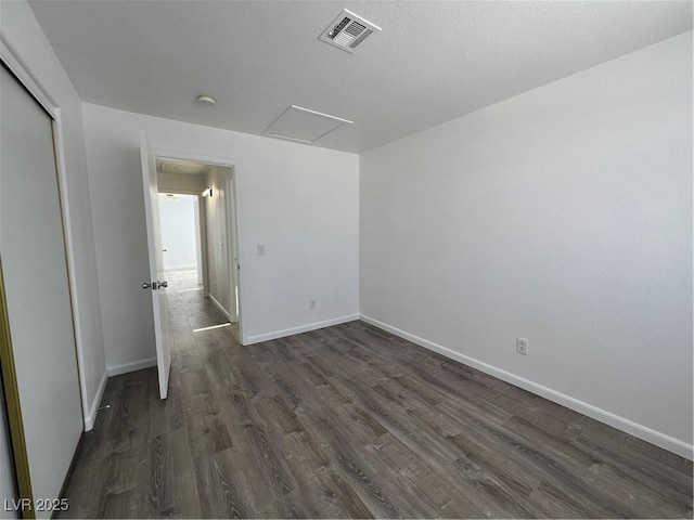 empty room with baseboards, dark wood-type flooring, visible vents, and attic access