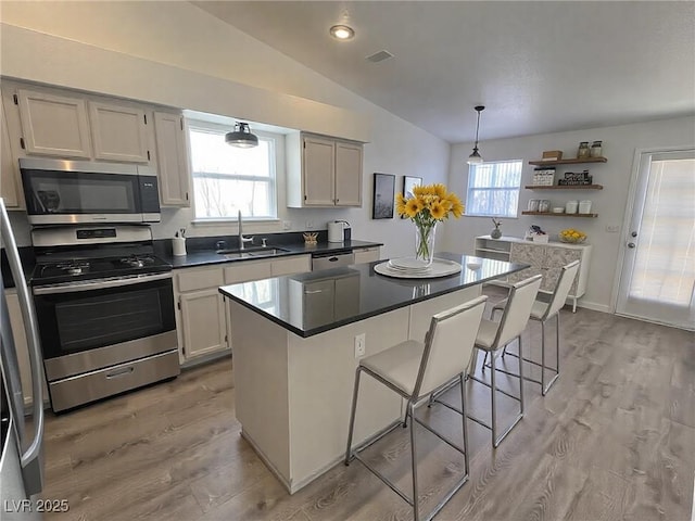 kitchen with stainless steel appliances, a sink, a center island, open shelves, and a kitchen bar